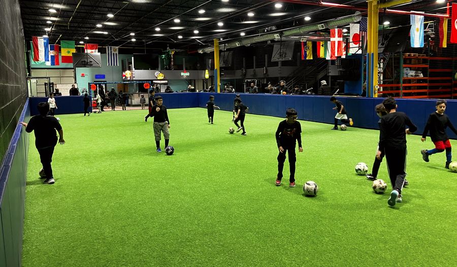 Boys dribbling soccer balls across an indoor turf field.